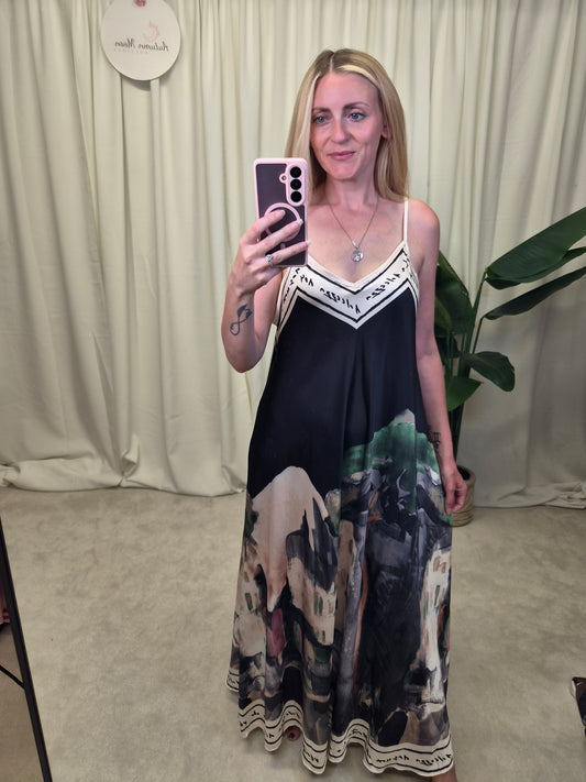 Vespera Landscape Print Slip Maxi Dress — black spaghetti strap maxi dress with landscape scene print at hem and script border trim